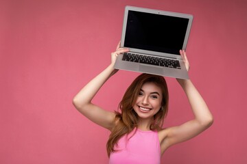 Photo of beautiful smiling young lady holding computer laptop looking at camera isolated over colourful background