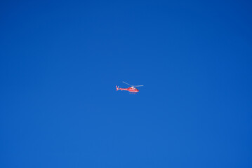 Red helicopter up in the sky on a beautiful summer day with blue sky background at Jungfrau Region. Photo taken July 20th, 2021, Lauterbrunnen, Switzerland.