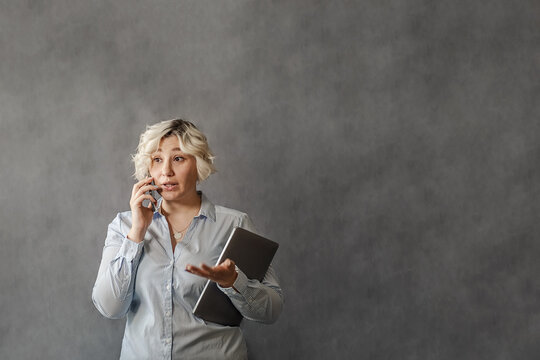 attractive young blonde talking on a mobile phone on a gray background, plus-size model, the concept of remote work online