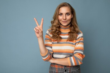 Photo of young positive happy smiling beautiful woman with sincere emotions wearing stylish clothes isolated over background with copy space and showing two fingers