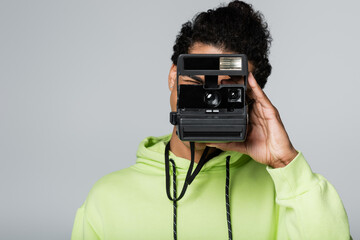 african american man in green hoodie taking photo on vintage camera isolated on grey