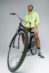 confident and stylish african american guy with bicycle looking at camera on grey background