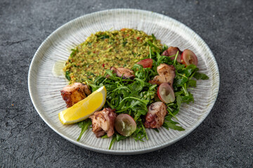 Grilled octopus salad, bulgur with spinach. Ready menu for the restaurant. Neutral gray blue textured background