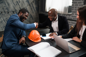 African American businessmen sit at the table and shake hands in honor of the conclusion of the deal