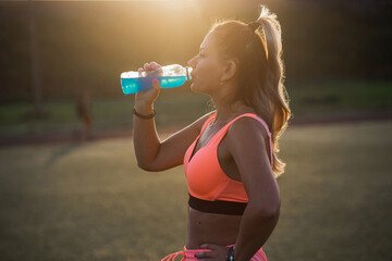 A woman is drinking water after training. A young and smiling girl is drinking a drink isotonic...