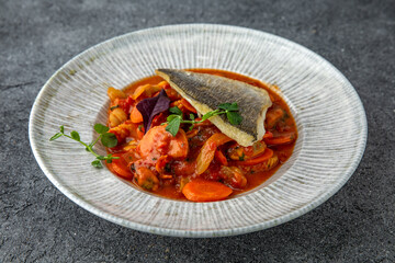 Dorada or sea bass on a pillow of stewed vegetables in sauce. Ready menu for the restaurant. Neutral gray blue textured background