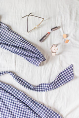Beauty fashion flat lay with women's vichy dress, wrist watch, beige earrings, lipstick and glasses on white cotton cloth. Top view fashion blog lifestyle concept