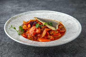 Dorada or sea bass on a pillow of stewed vegetables in sauce. Ready menu for the restaurant. Neutral gray blue textured background