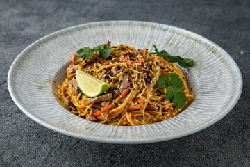 Thai soba with veal vegetables and sesame seeds. Ready menu for the restaurant. Neutral gray blue textured background