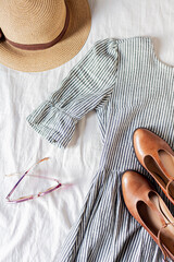 Beauty fashion flat lay with women's dress, a purse, brown shoes, a dried flower bouquet and sunglasses on white cotton cloth.  Top view fashion blog lifestyle concept.