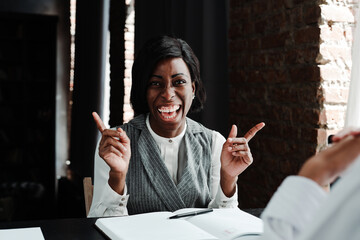Happy african american woman sitting at a table and having a job interview laughing and looking at the camera