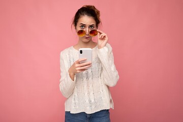 Photo of attractive crazy amazed surprised young woman wearing casual stylish clothes standing isolated over background with copy space holding and using mobile phone looking at camera