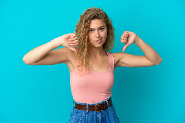 Young blonde woman isolated on blue background showing thumb down with two hands
