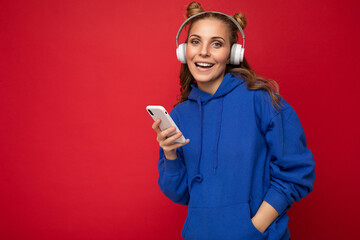 Photo of beautiful happy smiling young woman wearing stylish blue hoodie isolated over red...