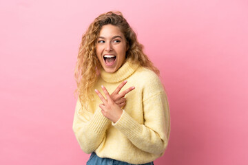 Young blonde woman isolated on pink background smiling and showing victory sign