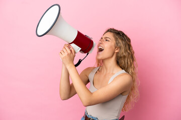 Young blonde woman isolated on pink background shouting through a megaphone to announce something...