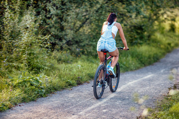 Naklejka premium A young woman riding a bicycle in a park in summer.