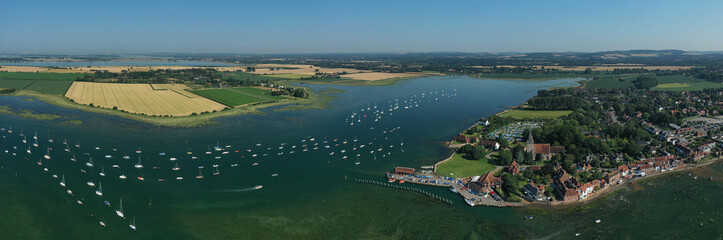 Bosham Village with boats moored in the estuary in the beautiful setting of the West Sussex countryside in Southern England. Aerial panoramic photo.