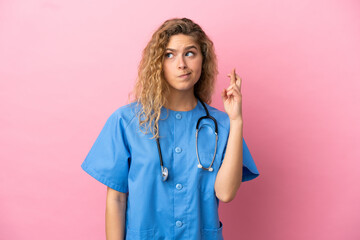 Young surgeon doctor woman isolated on pink background with fingers crossing and wishing the best