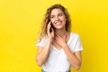 Fototapeta premium Young blonde woman using mobile phone isolated on yellow background looking up while smiling