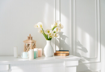 Soft home decor, white jug, vase with white and yellow beautiful flowers on a white wall background and on a wooden shelf. Interior.