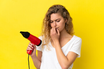 Young blonde woman holding a hairdryer isolated on yellow background having doubts