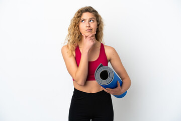 Young sport blonde woman going to yoga classes while holding a mat isolated on white background having doubts