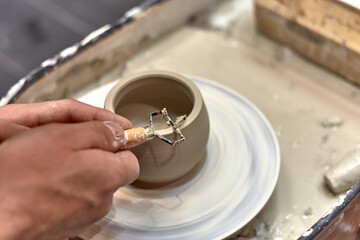 The hands of a man who learns to trim the edges of a product on a potter's wheel