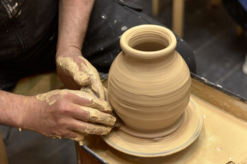 Fototapeta na wymiar Hands of a ceramist in the process of making a large vase of light clay on a potter's wheel