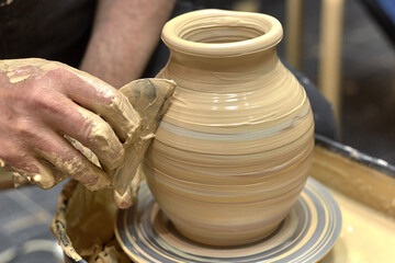 Hands of a ceramist in the process of leveling a finished vase of light clay on a potter's wheel using a specialized tool