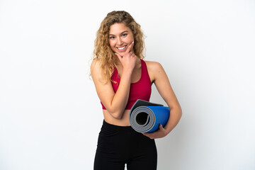Fototapeta premium Young sport blonde woman going to yoga classes while holding a mat isolated on white background happy and smiling