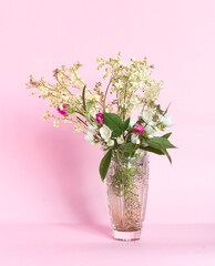 Bouquet of meadowsweet (Latin Filipndula), jasmine and wild roses in a vase on a pink background.	