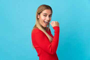 Young blonde woman isolated on blue background celebrating a victory