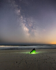 A person sitting alone on the beach under the Milky Way stretching across a dark sky. Long Island...