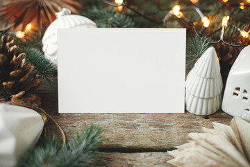 Empty greeting card and christmas paper stars, baubles, cones and pine branches in lights on rustic background. Christmas card mock up. Space for text. Seasons greetings template