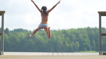 Woman jumping into the lake from wooden pier. Having fun on summer day on the vacations. Young girl diving in to the water from the dock. - Powered by Adobe