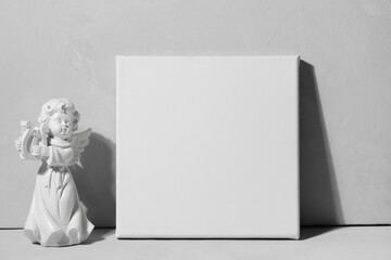 Blank canvas and angel figurine against grey wall. Mockup poster. White canvas, gallery wrap. Valentine day concept.