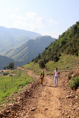 Obraz premium tourist family - mother and son hiking on mountain road to ancient abandoned village Gamsutl in Dagestan