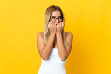 Young blonde woman isolated on yellow background nervous and scared putting hands to mouth