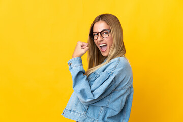 Young blonde woman isolated on yellow background celebrating a victory