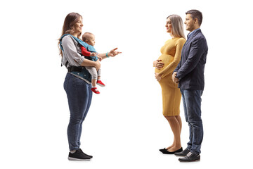 Fototapeta premium Full length profile shot of a mother with a baby in a carrier talking to a pregnant woman with her husband