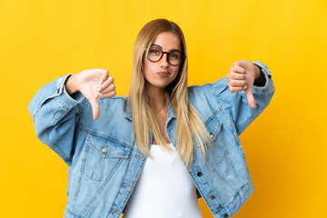 Young blonde woman isolated on yellow background showing thumb down with two hands
