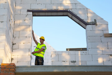 Construction worker at construction site measures the length of the window opening and the wall...