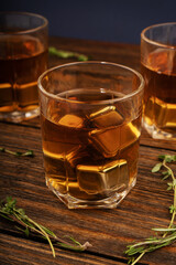 Glass with whiskey and metal ice cubes on a wooden table close-up.