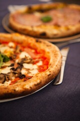 Close up. Two traditional Italian round pizzas with prosciutto, mushrooms, ham, pistachio, olives, basil and mozzarella cheese at the restaurant in Milan, Lombardy, Italy. European food and snacks. 