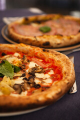 Close up. Two traditional Italian round pizzas with prosciutto, mushrooms, ham, pistachio, olives, basil and mozzarella cheese at the restaurant in Milan, Lombardy, Italy. European food and snacks. 