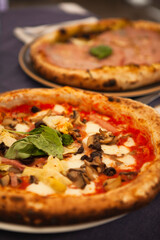 Close up. Two traditional Italian round pizzas with prosciutto, mushrooms, ham, pistachio, olives, basil and mozzarella cheese at the restaurant in Milan, Lombardy, Italy. European food and snacks. 