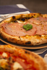 Close up. Traditional Italian round pizza with prosciutto and ham (mortadella), pistachio, basil and mozzarella cheese at the restaurant in Milan, Lombardy, Italy. European food and snacks. 