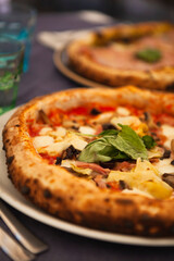 Close up. Two traditional Italian round pizzas with prosciutto, mushrooms, ham, pistachio, olives, basil and mozzarella cheese at the restaurant in Milan, Lombardy, Italy. European food and snacks. 
