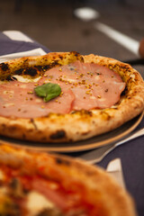 Close up. Traditional Italian round pizza with prosciutto and ham (mortadella), pistachio, basil and mozzarella cheese at the restaurant in Milan, Lombardy, Italy. European food and snacks. 